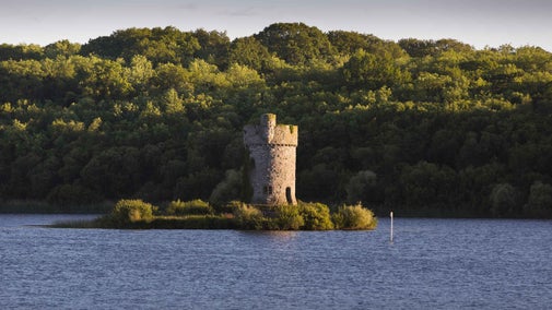 A view across Lough Erne to Crichton Tower standing on Gad Island, with trees in the background and a blue sky above